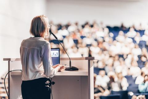 Nainen seisoo puhujakorokkeen takana pitäen esitystä seminaariyleisölle.