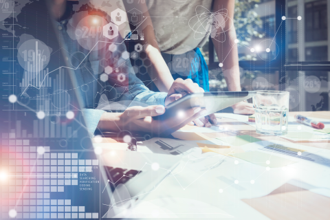 Kuvassa kaksi henkilöä työpöydän äärellä. Kuvassa grafiikkaa, joka kuvastaa tutkimusta, kuten prosenttilukuja ja kasvukäyriä.